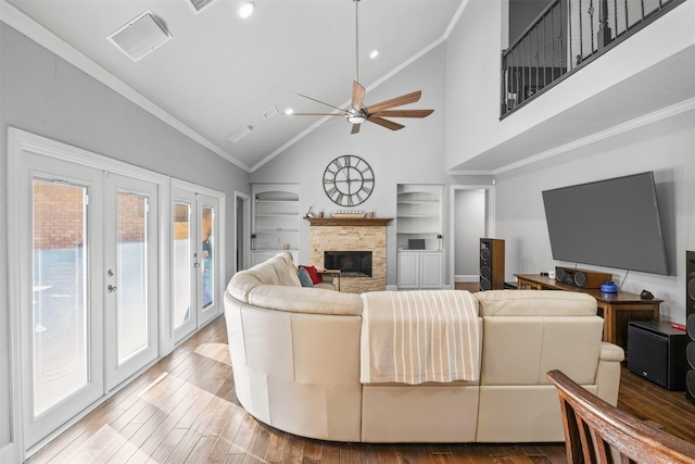 living room with french doors, built in shelves, lofted ceiling, a stone fireplace, and ornamental molding