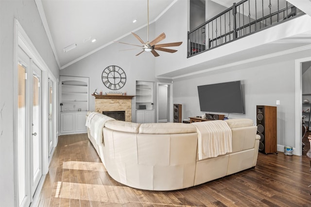 living room with built in shelves, ceiling fan, crown molding, a fireplace, and hardwood / wood-style floors