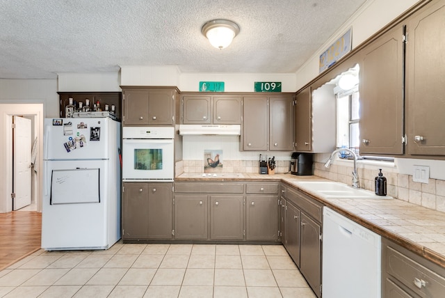 kitchen featuring sink, tasteful backsplash, a textured ceiling, tile counters, and white appliances