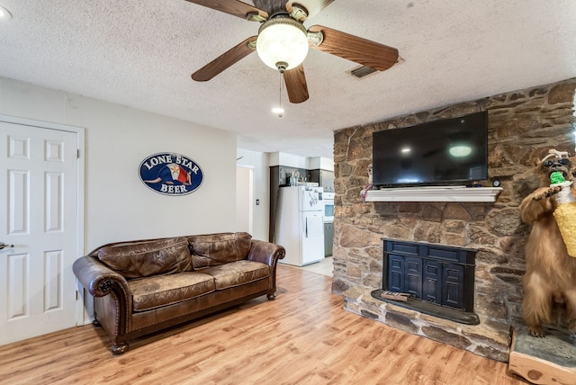 living room featuring ceiling fan, a fireplace, light hardwood / wood-style flooring, and a textured ceiling