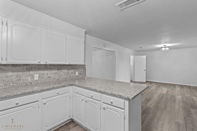 kitchen with white cabinets, decorative backsplash, hardwood / wood-style flooring, kitchen peninsula, and light stone countertops