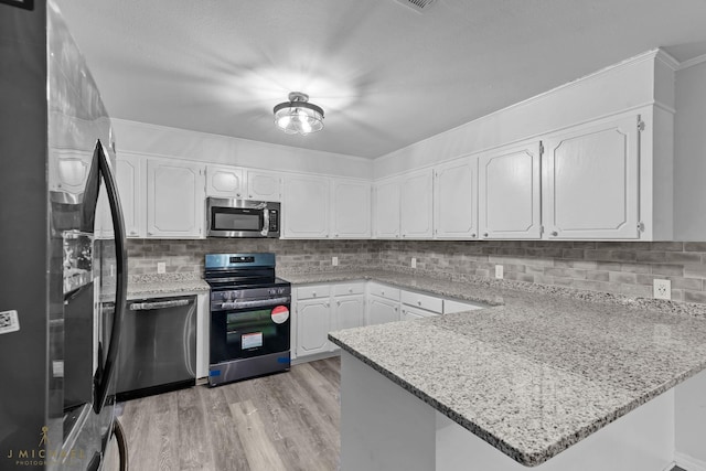 kitchen featuring appliances with stainless steel finishes, white cabinetry, decorative backsplash, kitchen peninsula, and light stone countertops