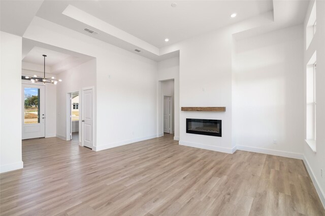 unfurnished living room featuring a high ceiling, light wood-type flooring, a tray ceiling, and a notable chandelier