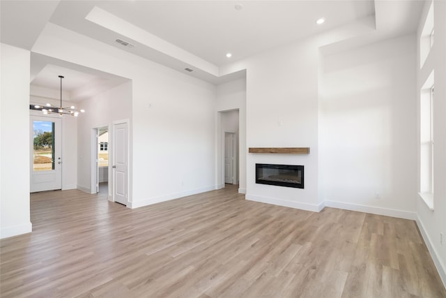 unfurnished living room featuring an inviting chandelier, a towering ceiling, a raised ceiling, and light hardwood / wood-style flooring