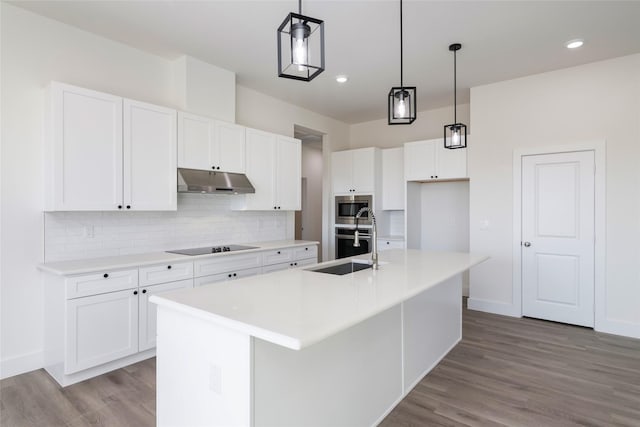 kitchen with appliances with stainless steel finishes, pendant lighting, white cabinets, decorative backsplash, and a center island with sink