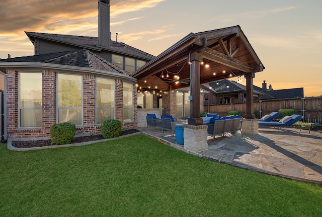 back house at dusk with outdoor lounge area, a yard, and a patio