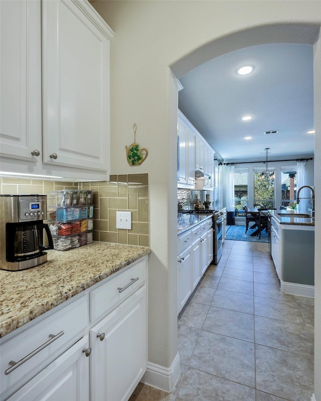 kitchen with tasteful backsplash, stainless steel gas range oven, and white cabinetry