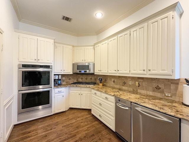 kitchen with dark wood-type flooring, ornamental molding, stainless steel appliances, light stone countertops, and white cabinets