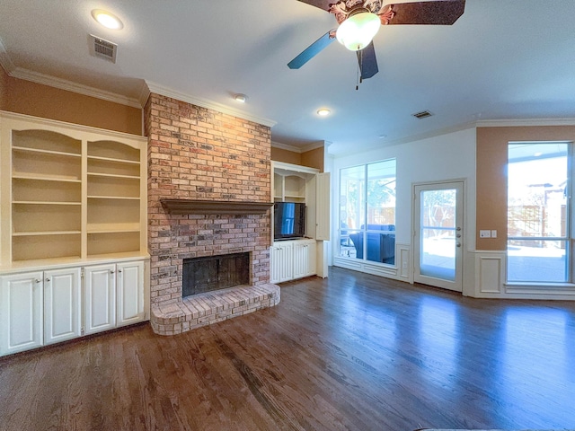 unfurnished living room with built in features, dark hardwood / wood-style flooring, ornamental molding, ceiling fan, and a brick fireplace