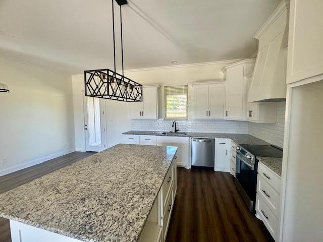 kitchen with dark wood-type flooring, white cabinets, appliances with stainless steel finishes, decorative light fixtures, and a kitchen island