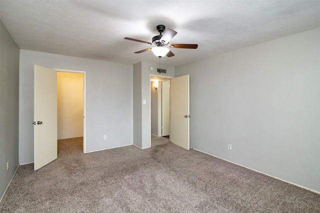 unfurnished bedroom featuring a walk in closet, ceiling fan, and carpet