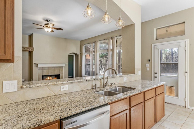 kitchen featuring pendant lighting, a tile fireplace, sink, stainless steel dishwasher, and light stone counters