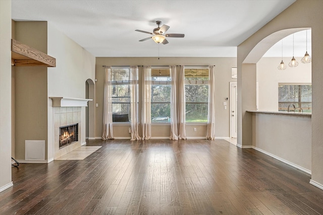 unfurnished living room with dark hardwood / wood-style flooring, ceiling fan, and a tiled fireplace