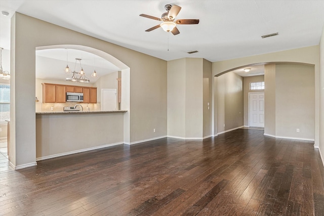 unfurnished living room featuring vaulted ceiling, ceiling fan with notable chandelier, and dark hardwood / wood-style floors