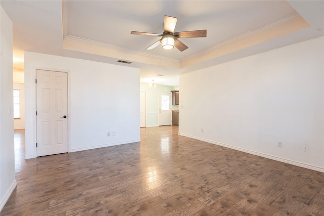 empty room with crown molding, a tray ceiling, dark hardwood / wood-style floors, and ceiling fan