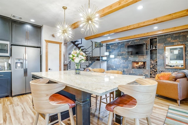 kitchen featuring appliances with stainless steel finishes, pendant lighting, a kitchen bar, a center island, and light stone countertops