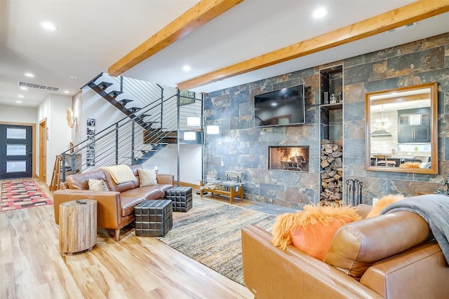 living room featuring beamed ceiling, wood-type flooring, and a tiled fireplace