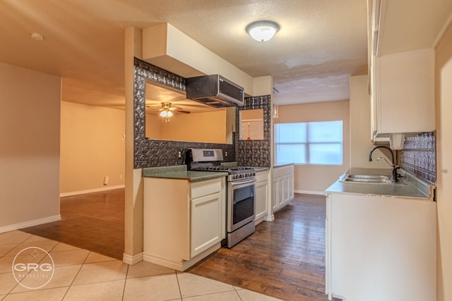 kitchen featuring sink, light tile patterned floors, stainless steel gas range, extractor fan, and white cabinets