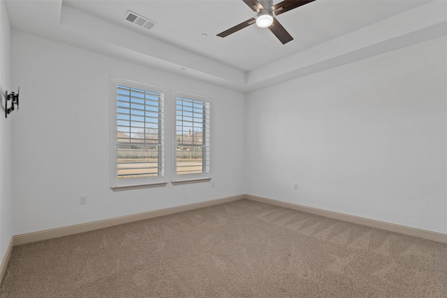 carpeted spare room with a raised ceiling and ceiling fan