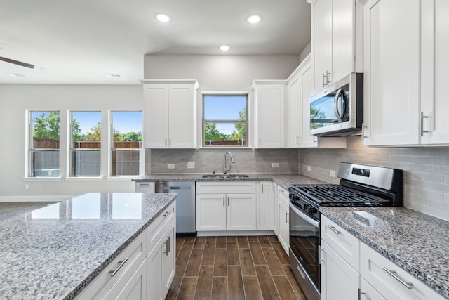 kitchen with backsplash, white cabinets, sink, appliances with stainless steel finishes, and light stone counters