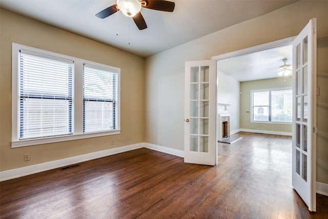 empty room with a fireplace, french doors, dark hardwood / wood-style flooring, and ceiling fan