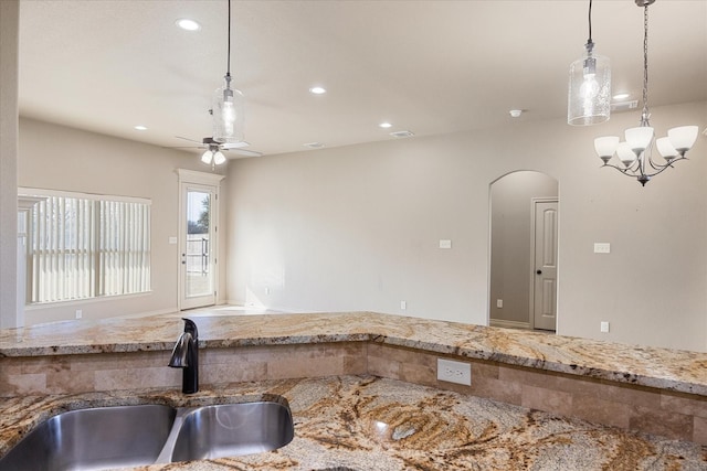 kitchen with light stone countertops, sink, ceiling fan with notable chandelier, and decorative light fixtures