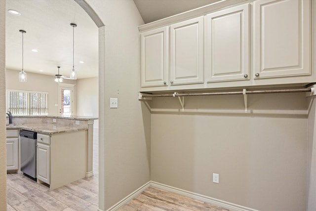 kitchen featuring light stone countertops, stainless steel dishwasher, ceiling fan, decorative light fixtures, and light hardwood / wood-style floors