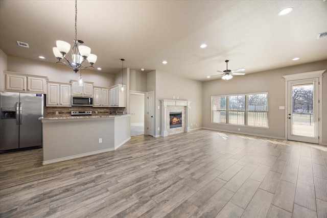 kitchen with ceiling fan with notable chandelier, hanging light fixtures, light stone countertops, light hardwood / wood-style floors, and stainless steel appliances