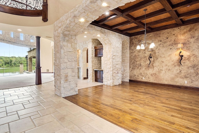 interior space with coffered ceiling, wood ceiling, an outdoor stone fireplace, beam ceiling, and a notable chandelier