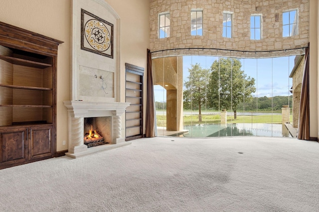 unfurnished living room with carpet, a towering ceiling, a water view, and exterior fireplace