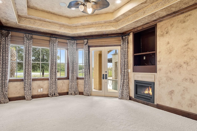 unfurnished living room with a tray ceiling, ceiling fan, french doors, and carpet floors