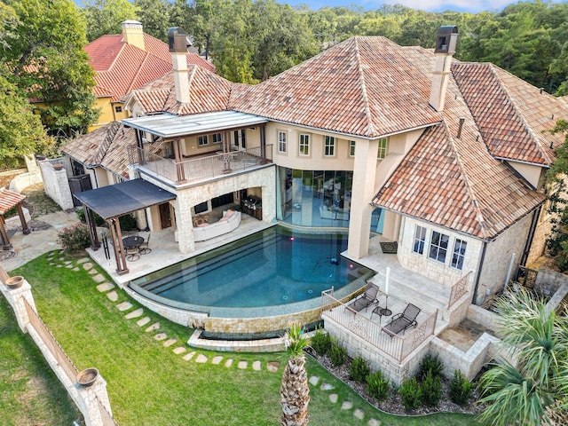 back of property with a fireplace, a yard, a patio, and a balcony