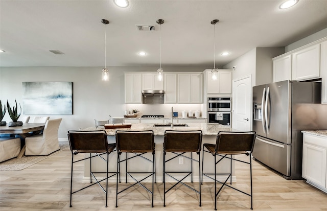 kitchen with an island with sink, white cabinetry, hanging light fixtures, stainless steel appliances, and light stone countertops