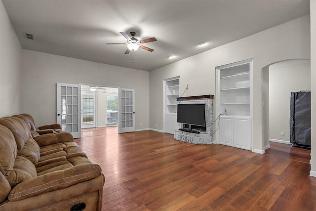 living room with ceiling fan, dark hardwood / wood-style floors, a brick fireplace, built in shelves, and french doors