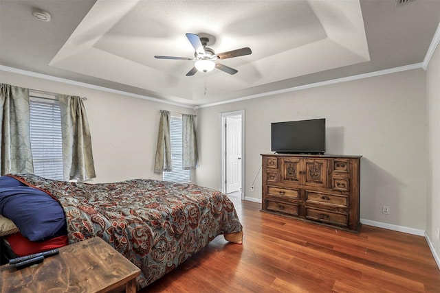 bedroom featuring dark hardwood / wood-style flooring, a tray ceiling, ornamental molding, and ceiling fan