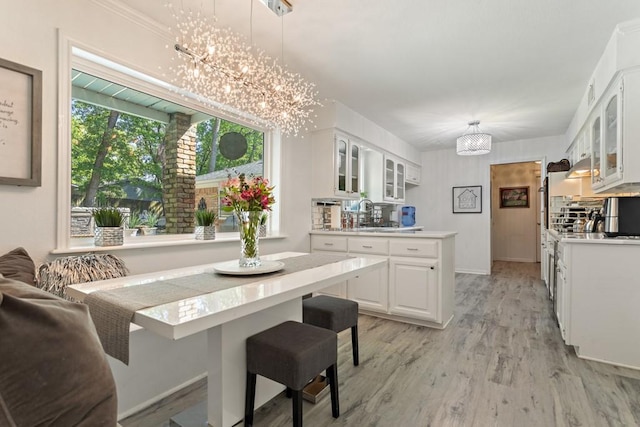 kitchen featuring a kitchen breakfast bar, pendant lighting, a chandelier, white cabinets, and light hardwood / wood-style floors