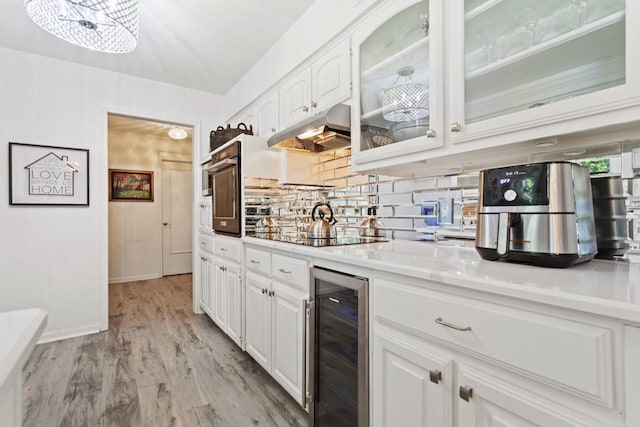 kitchen featuring wine cooler, backsplash, white cabinets, black appliances, and light wood-type flooring