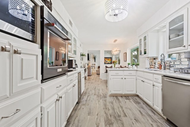 kitchen featuring appliances with stainless steel finishes, light wood-type flooring, sink, pendant lighting, and white cabinetry