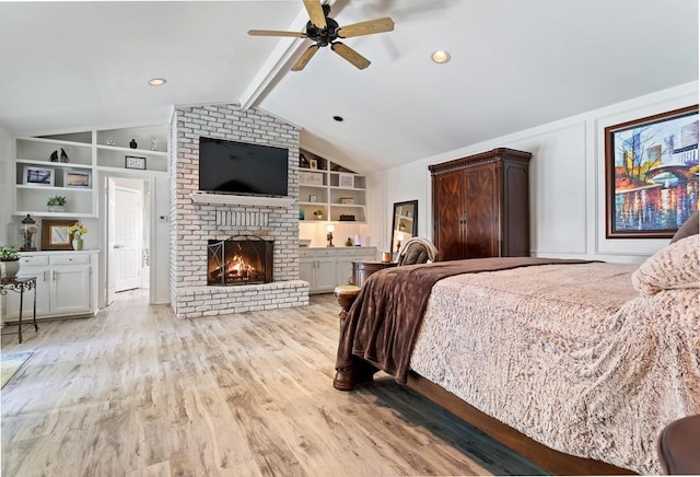 bedroom with vaulted ceiling with beams, ceiling fan, a brick fireplace, and light hardwood / wood-style flooring