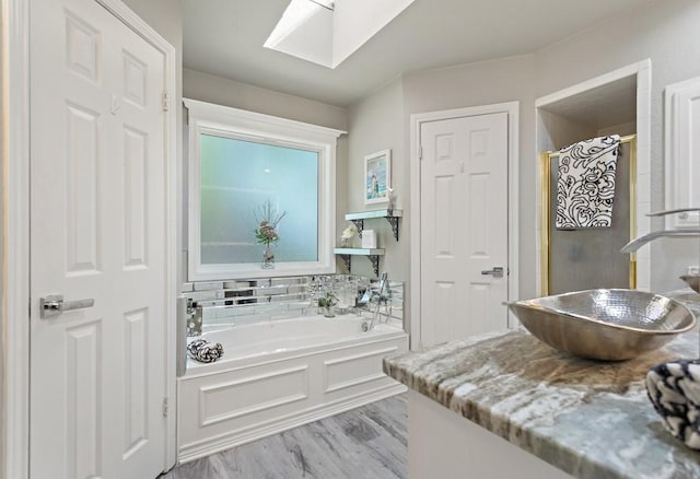 bathroom with a bath, hardwood / wood-style floors, vanity, and a skylight