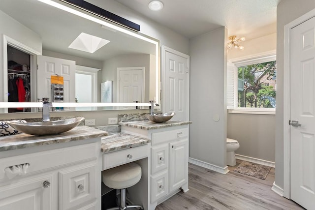 bathroom with hardwood / wood-style floors, vanity, toilet, and a skylight