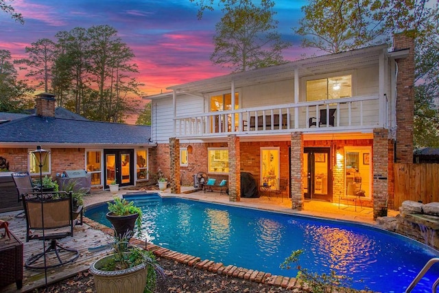 back house at dusk with french doors, a patio, and a balcony