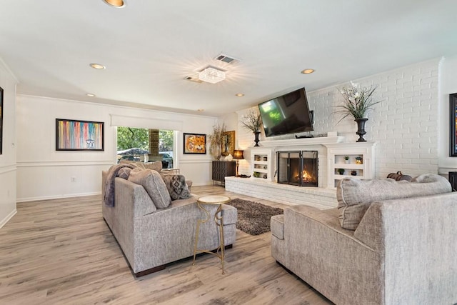 living room with light wood-type flooring, ornamental molding, and a brick fireplace