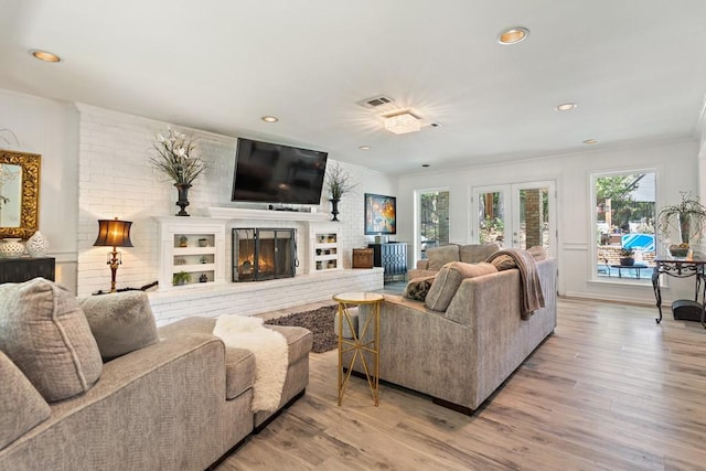 living room with a fireplace, french doors, light wood-type flooring, and crown molding