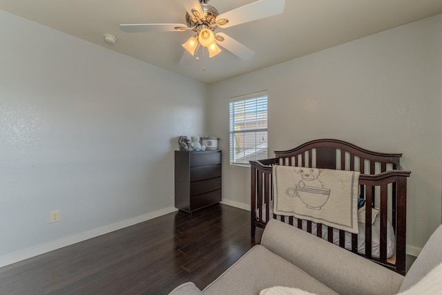 bedroom with a nursery area, ceiling fan, and dark wood-type flooring