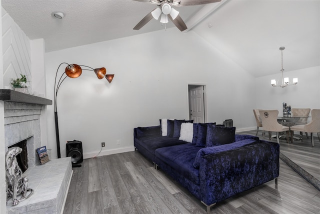 living room with a brick fireplace, vaulted ceiling with beams, hardwood / wood-style floors, a textured ceiling, and ceiling fan with notable chandelier