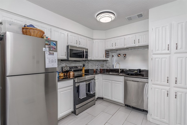 kitchen with sink, light tile patterned floors, a textured ceiling, appliances with stainless steel finishes, and white cabinetry