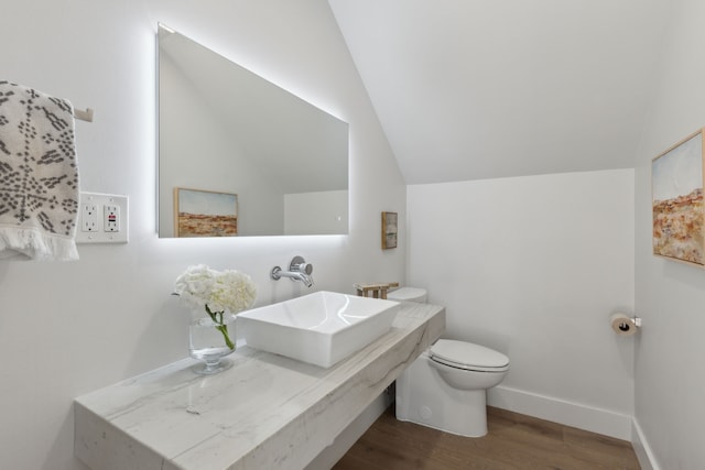 bathroom with hardwood / wood-style floors, toilet, sink, and vaulted ceiling