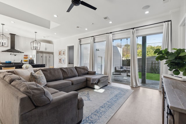 living room with ceiling fan with notable chandelier, crown molding, and light hardwood / wood-style flooring