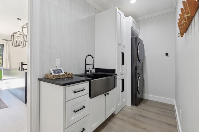 kitchen with ornamental molding, sink, decorative light fixtures, white cabinets, and stacked washer / drying machine